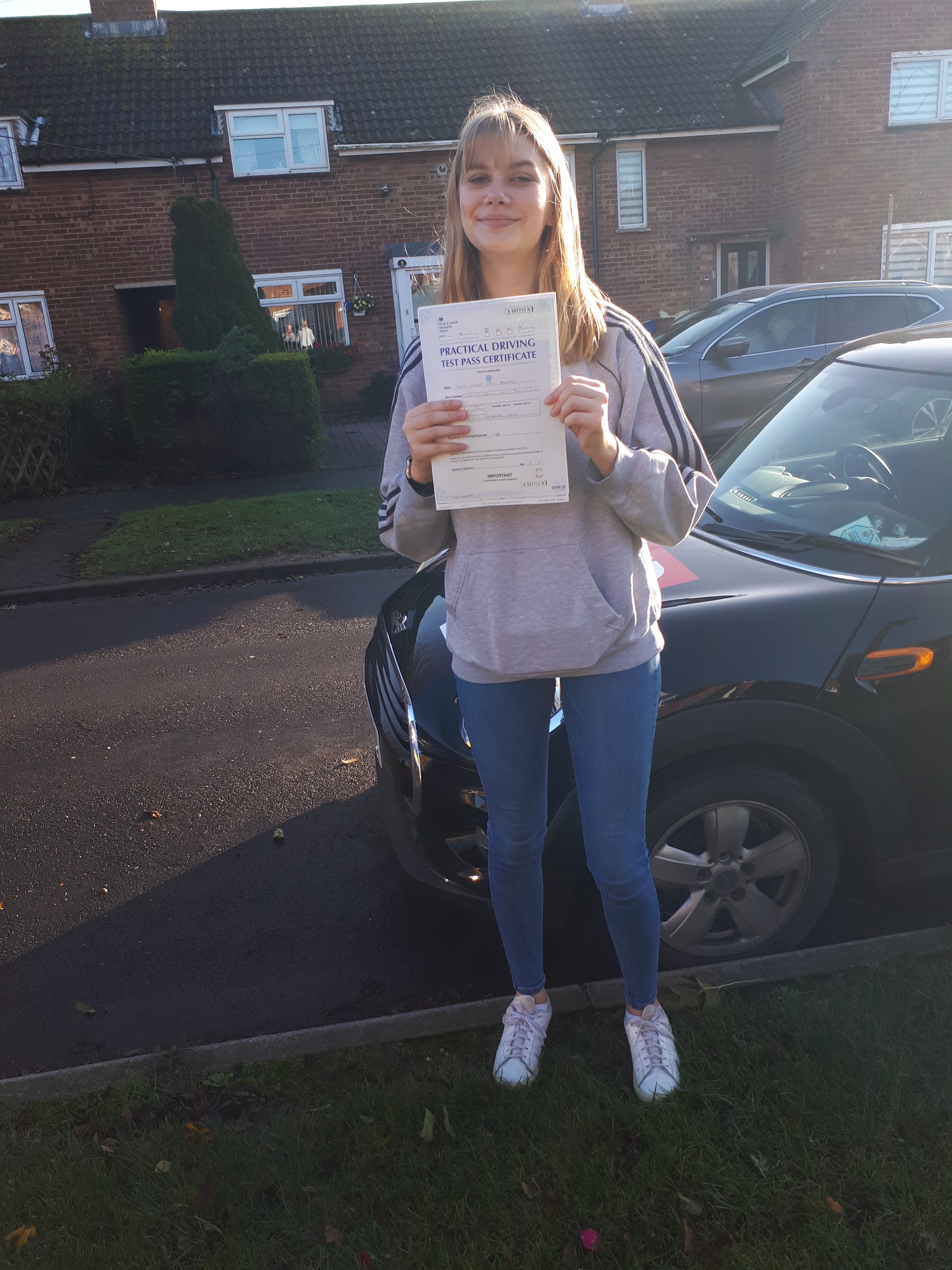 Girl holding her pass certificate after passing her driving test at Ashford kent test centre standing in front of a car