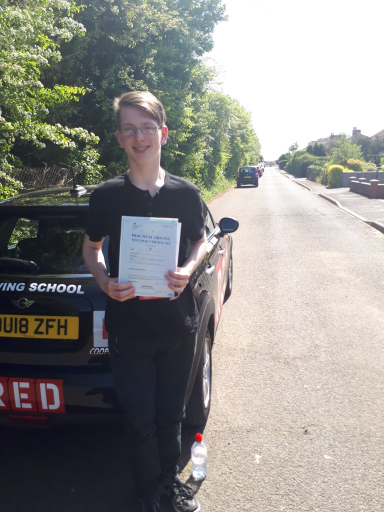 Boy holding driving test pass certificate standing next to a car