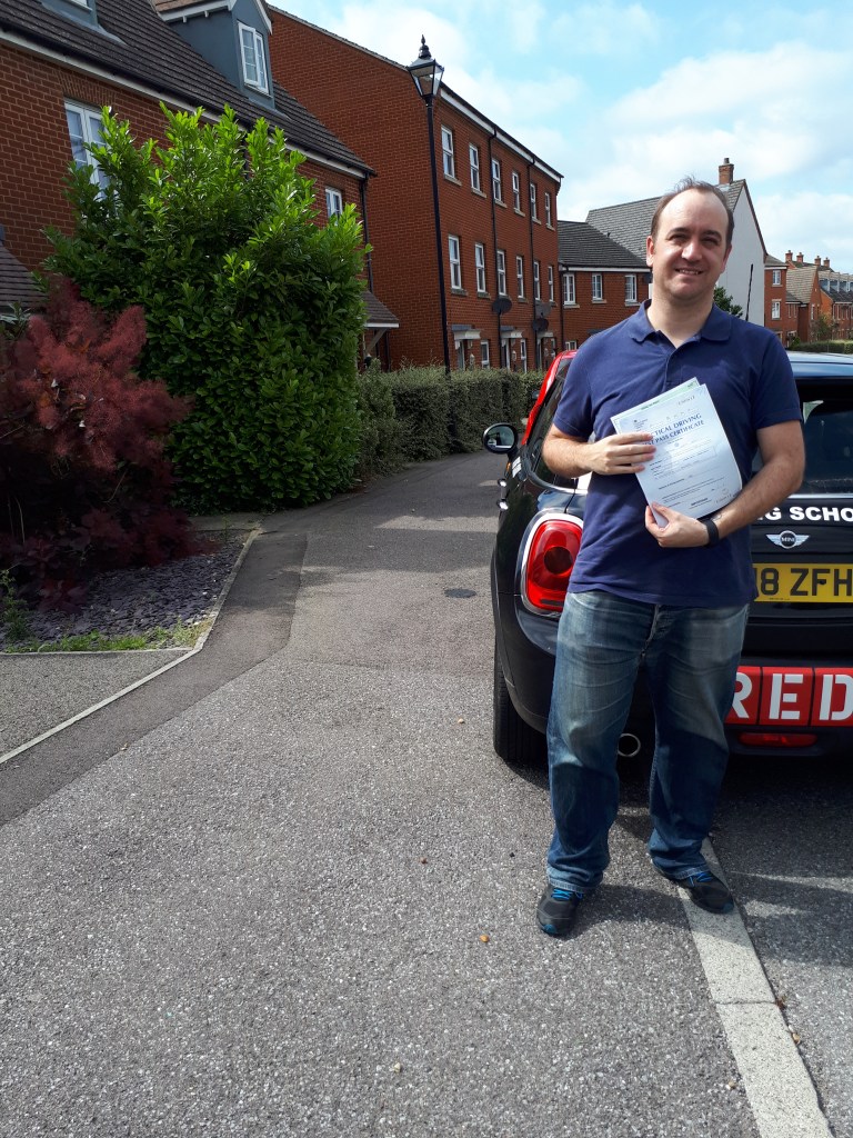 Man standing next to a car holding driving pass certificate, very happy