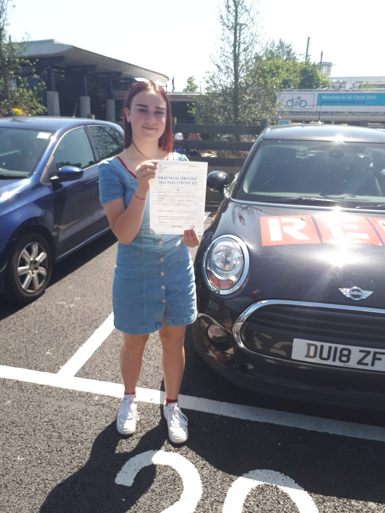Girl holding driving pass certificate standing in front of a mini cooper D