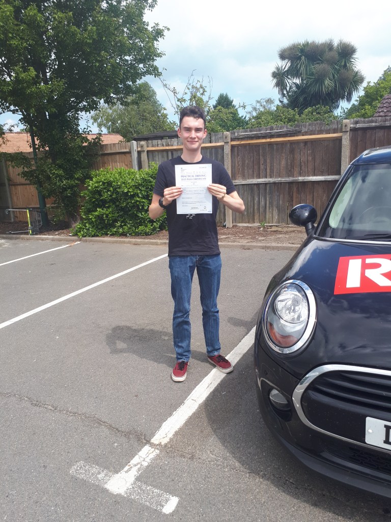 Boy standing holding a driving pass certificate next to a Mini Cooper